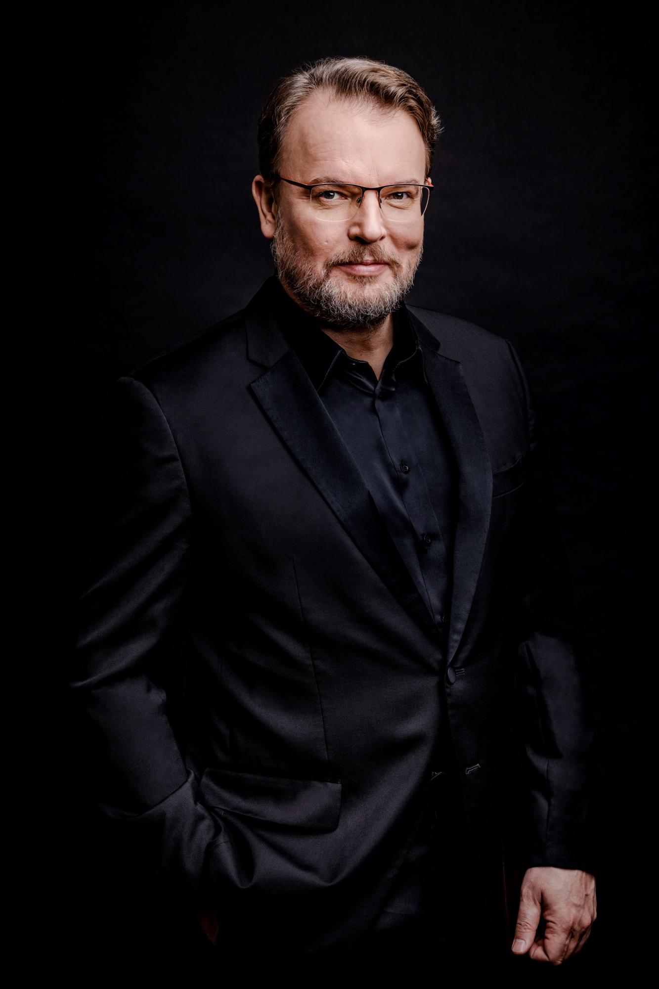 Śpiewak Tomasz Konieczny pozuje do zdjęcia, jest ubrany w czarny strój i nosi okulary